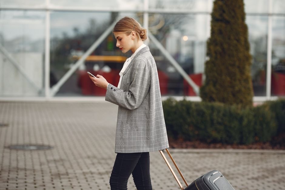 A traveller with a suitcase checking her phone outside an airport terminal