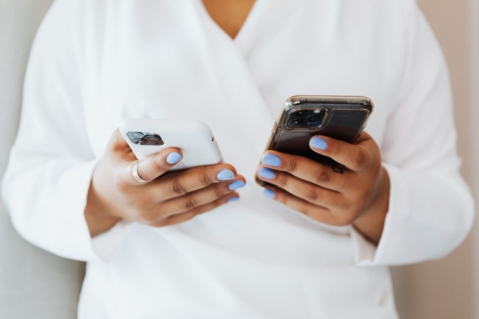 Une personne tient un iPhone dans une main et un autre smartphone dans l’autre