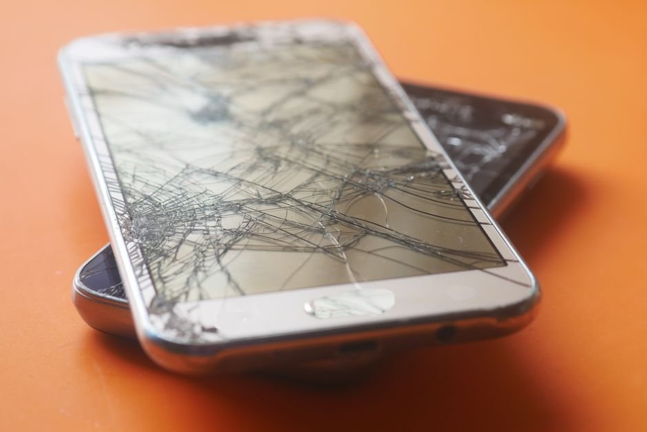 Two smartphones with shattered screens on an orange background